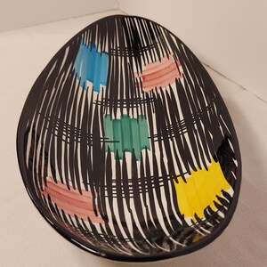 May include: A black oval ceramic serving dish with a white background and a geometric pattern of black lines and colourful squares in shades of blue, pink, green, and yellow.