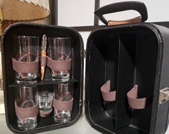 May include: A vintage black leatherette bar set, open to show glassware and a cocktail tool. The set includes four tall glasses, a small shot glass, and a cocktail tool, all secured with brown straps. The case has a handle for easy transport.