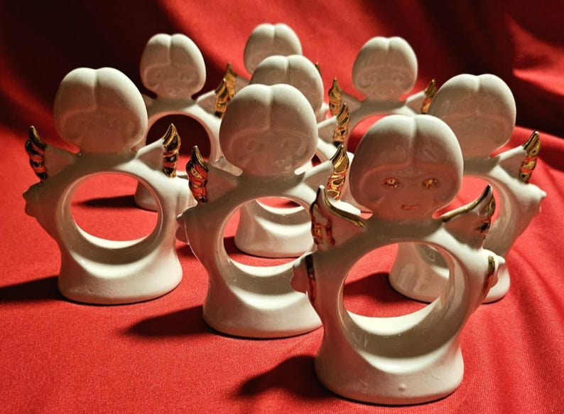 May include: Set of ten white ceramic angel napkin rings with gold accents. Each ring features a sculpted angel with wings and a halo.