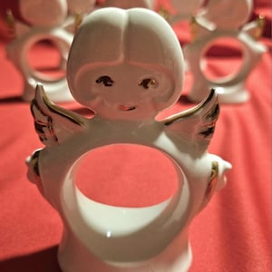 May include: Set of six white porcelain angel napkin rings with gold accents. Each ring features a small angel with wings and a face.