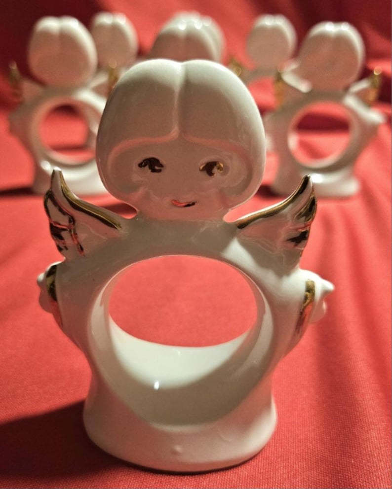 May include: Set of six white porcelain angel napkin rings with gold accents. Each ring features a small angel with wings and a face.