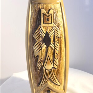 May include: A tan ceramic vase with a textured, rectangular design. The vase features a central relief with geometric shapes and a dark brown diamond. The vase is approximately 25 cm tall.