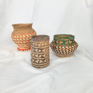 Peut inclure: Trois paniers tissés de formes et de tailles variées. Le plus grand est en forme de vase avec des accents orange et blancs. Le panier du milieu est cylindrique avec un motif géométrique. Le plus petit est en forme de bol avec des détails tissés verts, rouges et blancs.