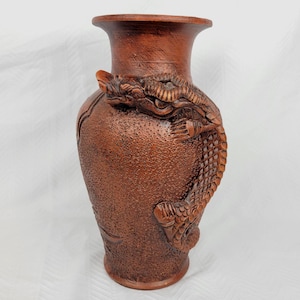 Peut inclure: Un vase en céramique marron avec une surface texturée et un relief en trois dimensions représentant un dragon enroulé autour du corps. Le vase présente un col effilé et un bord évasé, la tête du dragon étant située près du haut du récipient.