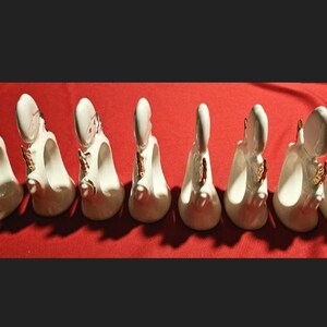 May include: Set of eight white ceramic napkin rings with gold accents. Each ring features a stylized angel design.