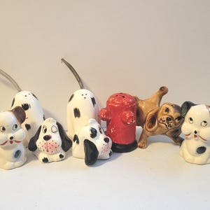 May include: A collection of ceramic dog figurines and salt and pepper shakers. The set includes various dog breeds in white, black, and brown, with a red fire hydrant shaker. The figurines are detailed and vintage.