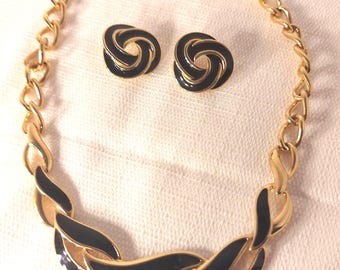 May include: A gold-tone metal necklace and matching pair of clip-on earrings. The necklace features a chain with a central section of interlocking, curved links filled with black enamel. The circular earrings feature a matching black enamel swirl.