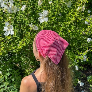 May include: A triangular head scarf featuring a vibrant pink and white striped knit pattern. The accessory is constructed with a textured, ribbed stitch design that creates a distinct diagonal visual effect across the fabric surface.