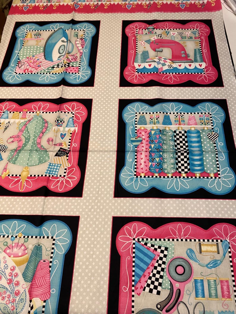 May include: A fabric panel featuring a repeating pattern of sewing-themed illustrations. Each illustration is framed with a black border and a pink or blue border. The illustrations include a sewing machine, spools of thread, a dress form, and sewing tools.