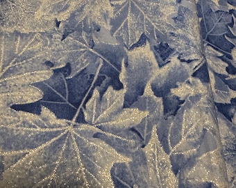 May include: Close-up of fabric with a repeating pattern of blue and silver maple leaves. The leaves have a glittery, shimmering effect, creating a textured and visually appealing design. The fabric is likely used for crafting or home decor.