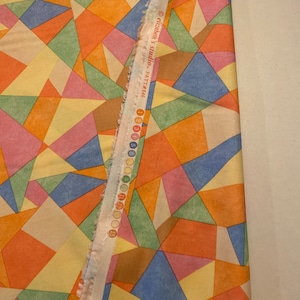 May include: A fabric with a geometric pattern of colorful triangles. The fabric is a light yellow with shades of orange, pink, blue, green, and brown. The fabric is labeled "elizabeth's studio - PATTI 4645".