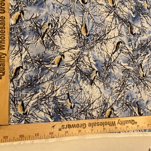 K&ouml;nnte beinhalten: Ein wei&szlig;er Stoff mit einem blauen und braunen Muster von V&ouml;geln in einem schneebedeckten Wald. Der Stoff hat ein Lineal darauf mit der Aufschrift "Quality Wholesale Growers".