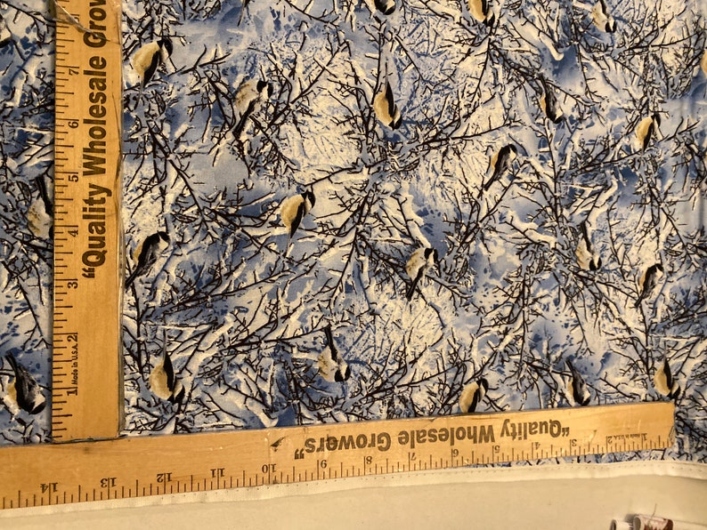 K&ouml;nnte beinhalten: Ein wei&szlig;er Stoff mit einem blauen und braunen Muster von V&ouml;geln in einem schneebedeckten Wald. Der Stoff hat ein Lineal darauf mit der Aufschrift "Quality Wholesale Growers".