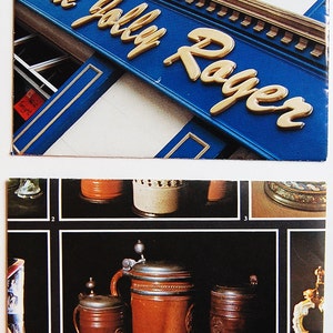 May include: A close-up of a vintage advertisement for The Jolly Roger pub. The sign is blue with gold lettering. The image also shows a collection of vintage beer steins with pewter lids.