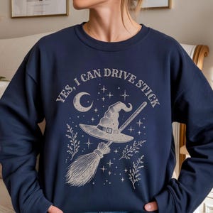 Può includere: Felpa blu navy con grafica a tema strega. Il design presenta un cappello da strega, una scopa, una luna, stelle e la scritta "YES, I CAN DRIVE STICK". Un top comodo ed elegante per Halloween o per tutti i giorni.