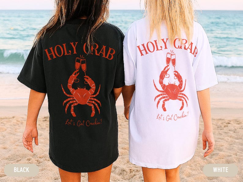 May include: Black and white t-shirts with a red crab graphic, champagne glasses, and the text "HOLY CRAB" and "Let's Get Crackin'!" on the back. The shirts are worn on a beach.