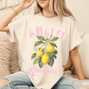 Pu&ograve; includere: Una maglietta bianca con una grafica rosa di limoni e il testo "Avalon Lemons" stampato sul davanti.