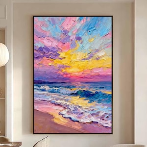 Puede incluir: Gran pintura al óleo enmarcada que representa una vibrante puesta de sol sobre una playa. La obra presenta pinceladas audaces en tonos rosa, amarillo, azul y morado, capturando el cielo, las olas y la arena. La pintura se exhibe en un interior moderno y bien iluminado.