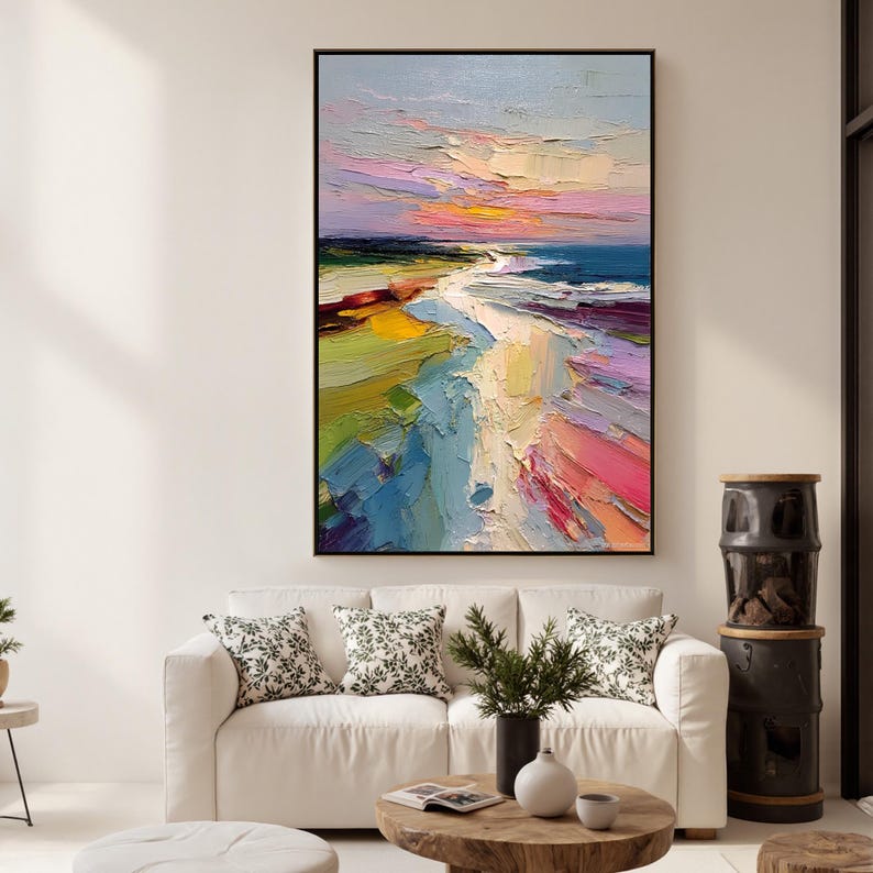 May include: An abstract oil painting of a coastal landscape. The artwork features a vibrant sunset with hues of pink, yellow, and orange. The foreground depicts a beach with strokes of white, yellow, and blue. The painting is framed in a black border.
