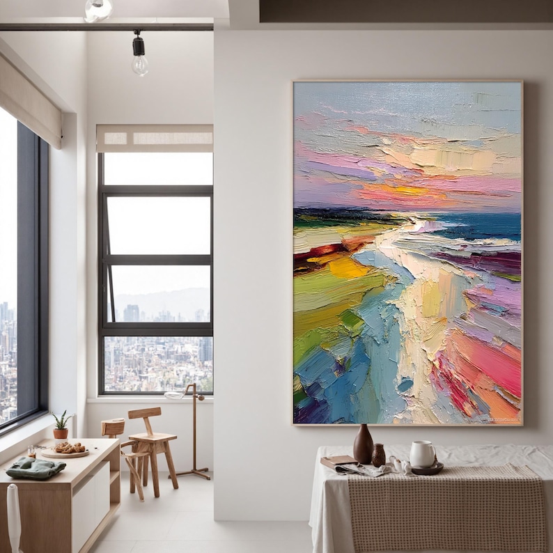 May include: An abstract oil painting of a beach scene with a colorful sunset. The artwork features thick brushstrokes in shades of blue, green, yellow, pink, and purple. The painting is framed and hangs on a white wall.