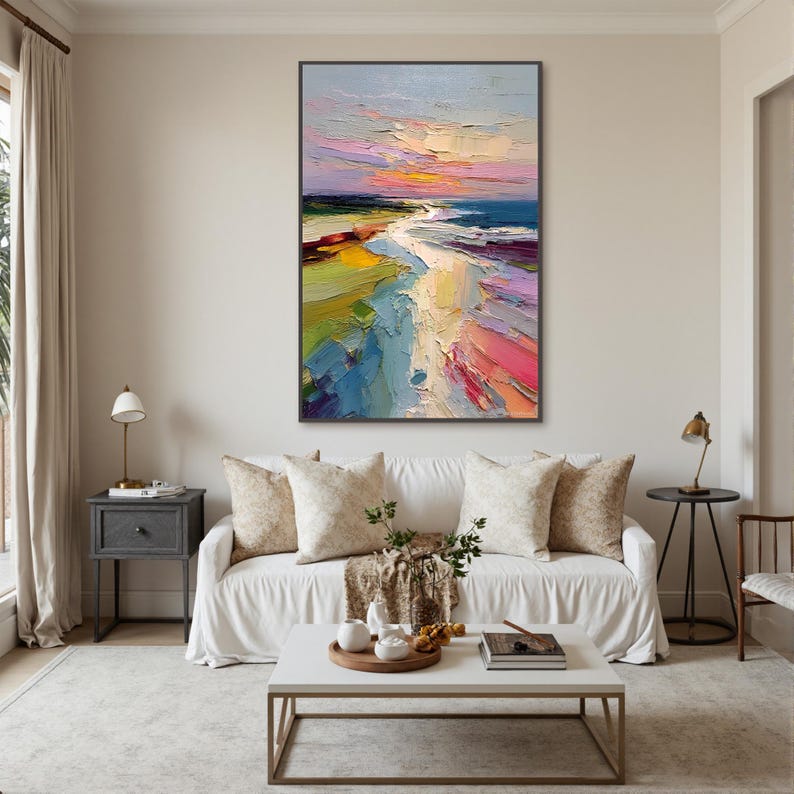 May include: A large, rectangular abstract painting with a beach scene. The artwork features a vibrant palette of colors, including blues, pinks, yellows, and greens. The painting is displayed above a white sofa with decorative pillows in a living room setting.