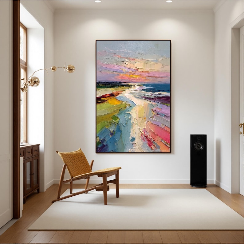 May include: An abstract landscape painting with a black frame. The artwork depicts a beach scene with a colorful sunset. The painting features vibrant brushstrokes in shades of blue, pink, yellow, and green. A wooden chair and a black speaker are in the room.