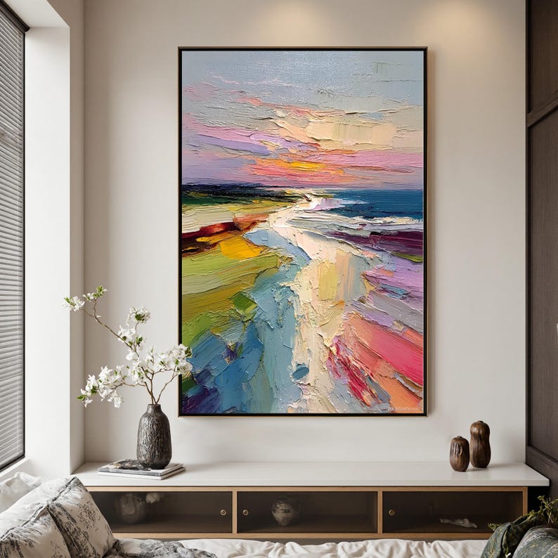 May include: Abstract landscape painting with a black frame. The artwork features a beach scene with a colorful sky in shades of pink, yellow, and blue. The textured brushstrokes create a dynamic and vibrant effect, with the ocean and sand in the foreground.