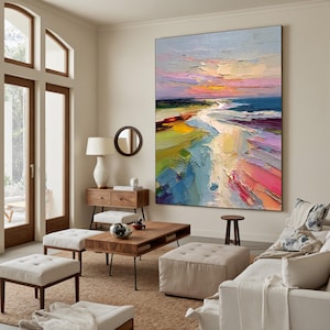 May include: Large, vertical abstract painting depicting a beach scene at sunset. The artwork features bold brushstrokes and a vibrant palette of blues, pinks, yellows, and greens, creating a textured and dynamic composition. The painting is displayed in a living room setting.