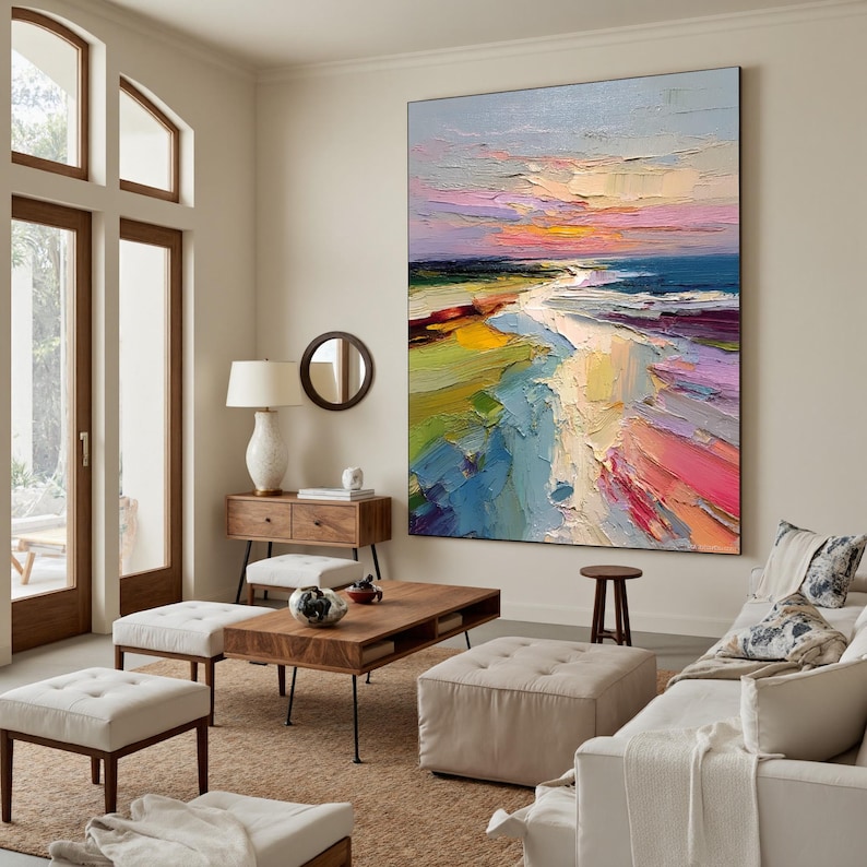 May include: Large, vertical abstract painting depicting a beach scene at sunset. The artwork features bold brushstrokes and a vibrant palette of blues, pinks, yellows, and greens, creating a textured and dynamic composition. The painting is displayed in a living room setting.