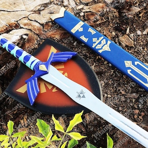 May include: A replica sword, shield, and scabbard set. The sword has a silver blade and blue hilt with a light blue wrap. The shield is black with a red center and gold accents. The blue scabbard has gold designs.