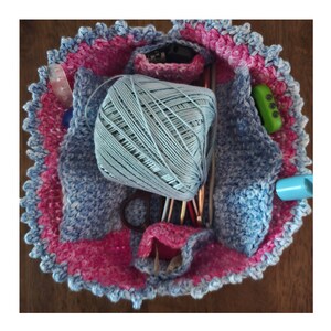May include: A crocheted project bag in pink and blue with a scalloped edge. The bag is filled with yarn, crochet hooks, and other supplies. It can be stored flat or folded to a 4 x 5 x 2 inch square.