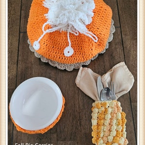 May include: Crocheted fall-themed kitchen accessories. A pumpkin-shaped pie carrier, a bowl holder, and a napkin holder with cutlery.
