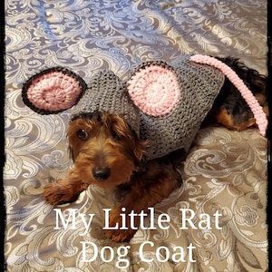 May include: A small brown dog wearing a gray and pink crocheted rat costume. The costume has a long tail and large ears. The dog is lying on a patterned bedspread. The text "My Little Rat Dog Coat" is written below the dog.