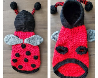 Può includere: Un costume da coccinella in crochet rosso e nero per un animale domestico. Il costume ha un cappuccio, ali e macchie nere.
