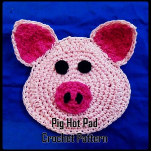 May include: Pink crocheted pig hot pad with black eyes and a pink snout. The hot pad has the text "Pig Hot Pad Crochet Pattern" at the bottom.