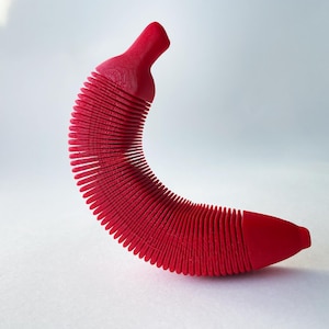 May include: A bright red, flexible, accordion-style banana-shaped object. The object is made of a textured material and is curved into a crescent shape.