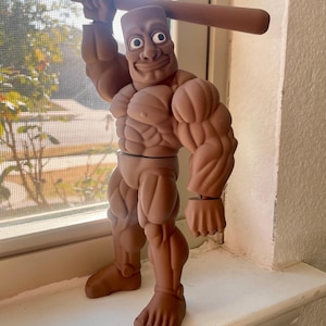 Könnte beinhalten: Eine braune, muskulöse Actionfigur mit einem lächelnden Gesicht und einem Baseballschläger über dem Kopf. Die Figur hat übertriebene Muskeln und posiert auf einer weißen Fensterbank. Der Hautton der Figur ist ein mittleres Braun.