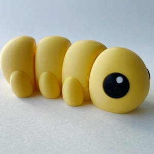 Puede incluir: Un juguete amarillo en forma de oruga segmentado con ojos negros y un punto blanco en cada ojo.