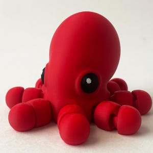 May include: A bright red octopus toy with eight tentacles. The octopus has a black eye and a white spot on its head.