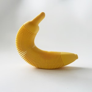 May include: A yellow rubber banana-shaped toy with a textured surface. The toy is made of multiple sections that can be compressed and extended.