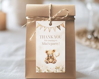 May include: A brown paper gift bag with a tag that reads "THANK YOU for coming to Mia's party!" The tag features a watercolour illustration of a teddy bear holding a balloon. The tag is adorned with a banner of small flags.