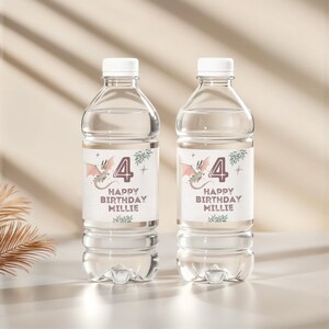 Könnte beinhalten: Zwei transparente Plastikwasserflaschen mit weißen Deckeln. Jede Flasche hat ein Etikett mit einer Drachengrafik, der Zahl 4 und dem Text "HAPPY BIRTHDAY MILLIE". Der Drache ist rosa und grau. Die Flaschen stehen auf einer weißen Oberfläche.