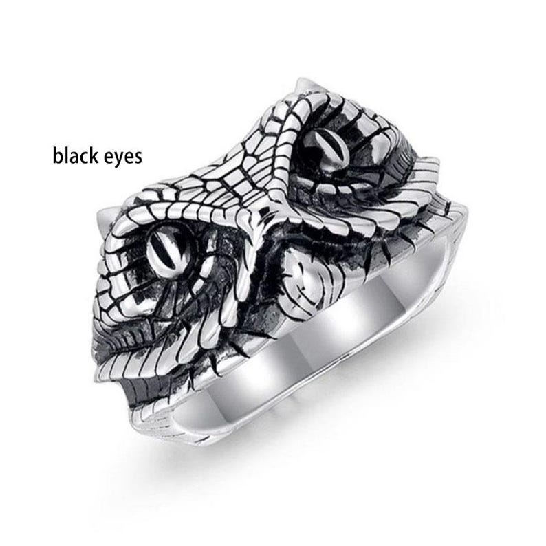 May include: A silver ring with a detailed snake head design. The snake's head is textured with scales and has black eyes. The ring has a polished finish and a wide band.