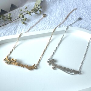 May include: Two gold and silver necklaces with personalized names "Eleanor" and "Grace" on a white surface.