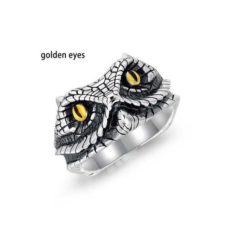 May include: Silver ring with a reptile head design. The ring has a textured surface with golden eyes and the text "golden eyes". A unique piece of jewellery.
