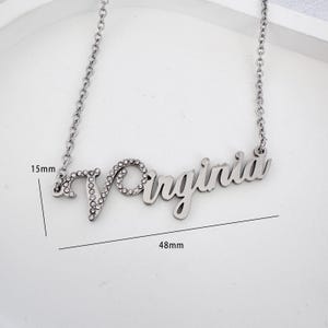 以下が含まれることがあります： 「Virginia」という名前が、ラインストーンで飾られた筆記体で書かれたシルバーネックレス。ネックレスの長さは48mm、幅は15mmです。