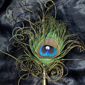 Pu&ograve; includere: Una piuma di pavone con un designo di filo dorato, attaccato a una penna in metallo dorato. La piuma &egrave; verde, blu e marrone con un occhio bianco iridescente.