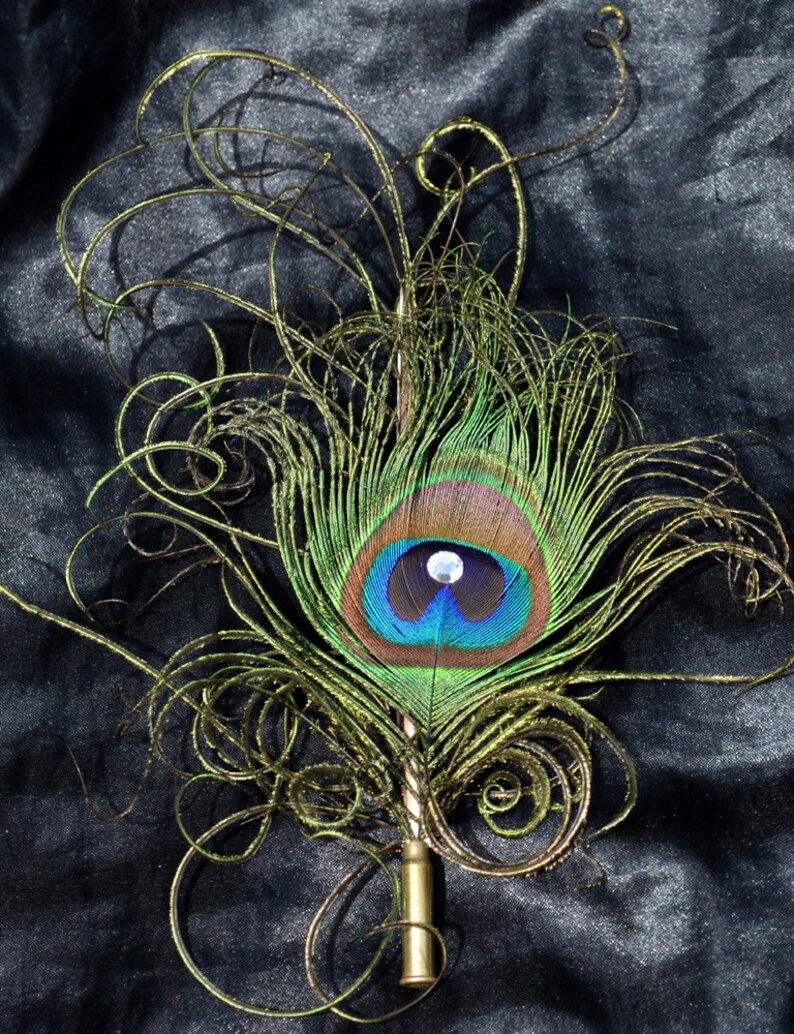 Pu&ograve; includere: Una piuma di pavone con un designo di filo dorato, attaccato a una penna in metallo dorato. La piuma &egrave; verde, blu e marrone con un occhio bianco iridescente.