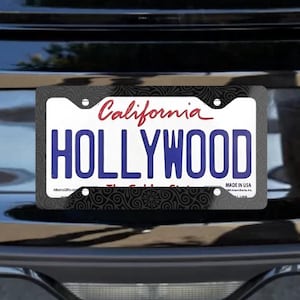 Puede incluir: Parte trasera de un coche negro con un marco de matrícula. La matrícula dice "HOLLYWOOD" en letras azules, con "California" en escritura roja. El marco tiene un patrón decorativo. Un emblema plateado de Mustang está arriba.