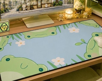 May include: A desk setup featuring a computer monitor displaying a Boba shop scene. A light blue mousepad with green frog illustrations and white flowers is in front of the monitor. A white mouse sits on the mousepad. Various decorative items surround the monitor.